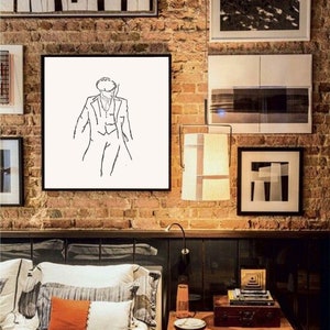 May include: Black and white line drawing of a person wearing a hat and suit, framed in a black frame and hanging on a brick wall above a bed with orange and white pillows.