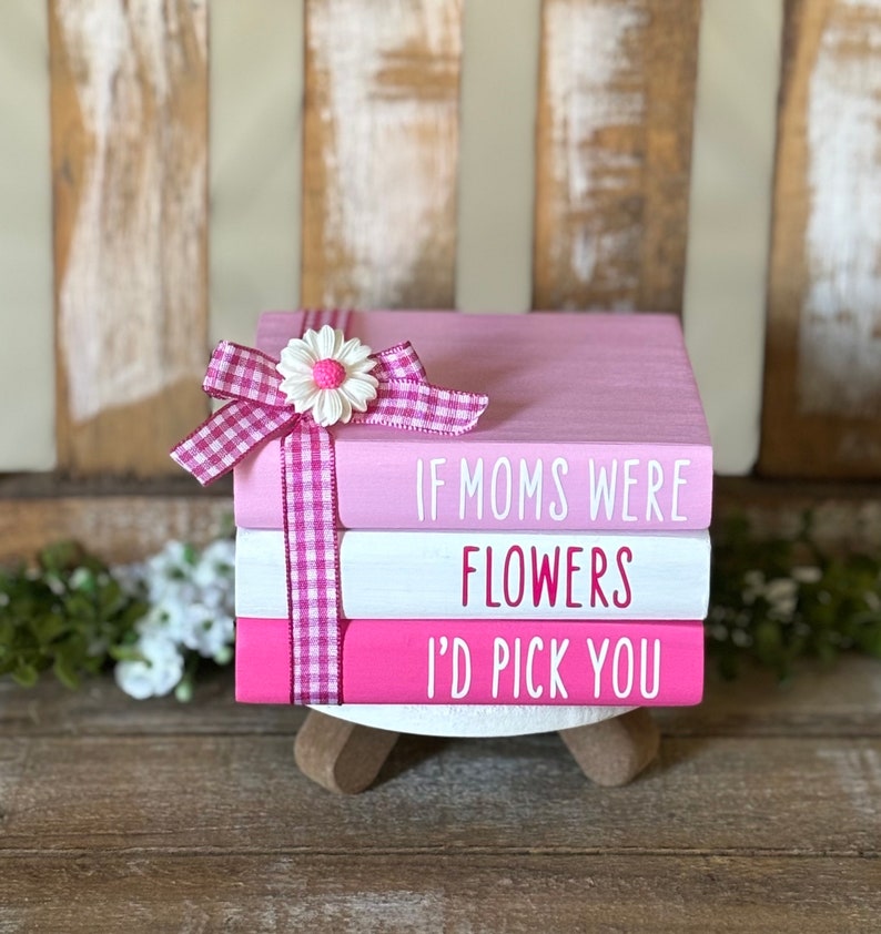 May include: Three pink and white stacked wooden blocks with the text "If moms were flowers I'd pick you" in pink lettering. The top block has a pink and white gingham ribbon with a white daisy.