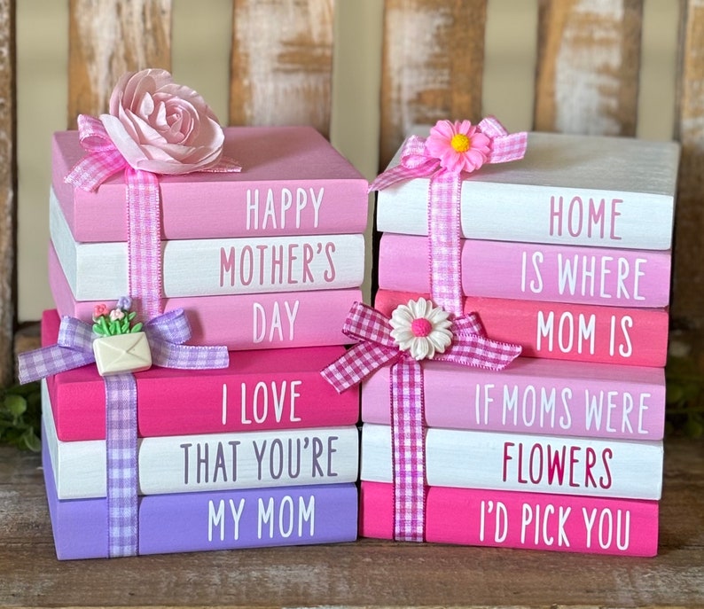 May include: A stack of pink and white wooden blocks with pink and white gingham ribbon. The blocks have the following text: "Happy Mother's Day", "I Love That You're My Mom", "Home Is Where Mom Is", "If Moms Were Flowers I'd Pick You".