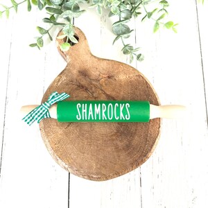 May include: Green rolling pin with a white "Shamrocks" inscription on a wooden chopping board.