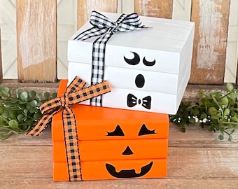 May include: A stack of three white wooden blocks with a ghost face painted on them, topped with a black and white checkered ribbon. Below the ghost blocks is a stack of three orange wooden blocks with a pumpkin face painted on them, tied with a black and orange checkered ribbon.