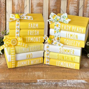 Puede incluir: Dos pilas de libros decorativos de madera pintados de amarillo y blanco, con texto y lazos con temática de limón. Los libros dicen "Farm Fresh Lemons", "Lemon Kisses and Summer Wishes", "Easy Peasy Lemon Squeezy" y "Summer Sunshine Lemonade".