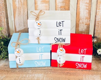 Könnte beinhalten: Drei Sätze gestapelter Holzblöcke mit dem darauf gemalten Spruch "Let it Snow". Jedes Set ist mit einer Schneemannfigur und einer Schnur verziert.