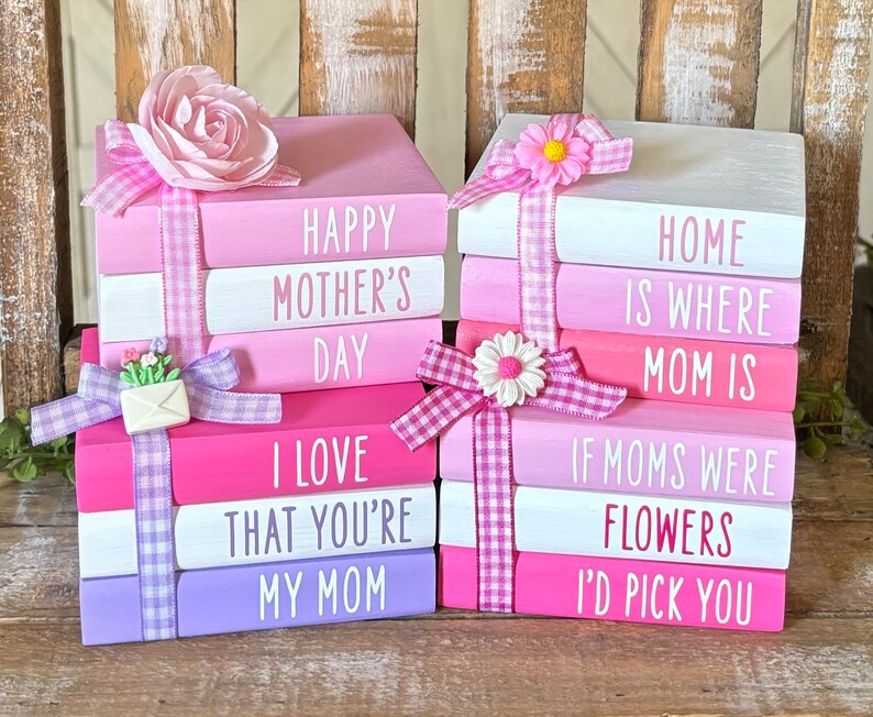 May include: Two stacks of painted wooden blocks with pink, white, and purple paint. The blocks are decorated with pink and white gingham ribbon, flowers, and the text "HAPPY MOTHER'S DAY I LOVE THAT YOU'RE MY MOM" and "HOME IS WHERE MOM IS IF MOMS WERE FLOWERS I'D PICK YOU".