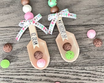 Puede incluir: Dos cucharones de helado de madera con cuentas y cinta de colores. Los cucharones están etiquetados como "Ice Cream" y "Mint Chocolate Chip".