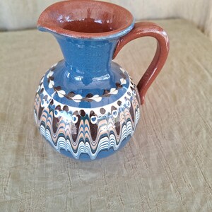 May include: A blue and brown ceramic pitcher with a wavy design. The pitcher has a brown handle and a brown rim.