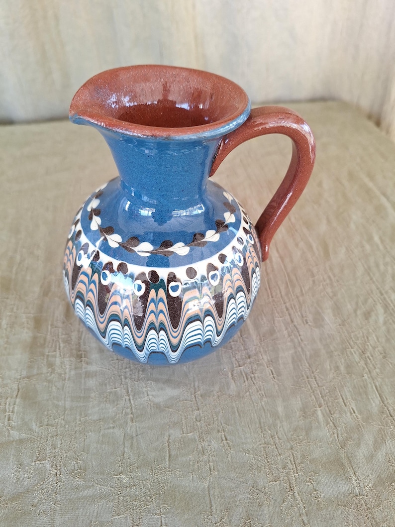 May include: A blue and brown ceramic pitcher with a wavy design. The pitcher has a brown handle and a brown rim.