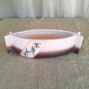 May include: A white ceramic planter with a brown glaze on the bottom half. The planter has a rounded shape and a raised lip around the top. It has Japanese characters written on the side that say "寿 壽".