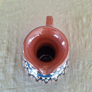 May include: A brown ceramic pitcher with a blue and white geometric pattern. The pitcher has a wide mouth and a handle.