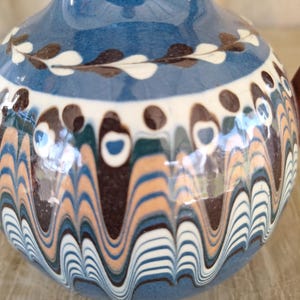 May include: A blue ceramic vase with a wavy pattern in shades of brown, white, and blue. The vase has a white rim and a brown and white floral design around the top.