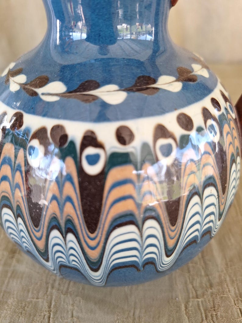May include: A blue ceramic vase with a wavy pattern in shades of brown, white, and blue. The vase has a white rim and a brown and white floral design around the top.
