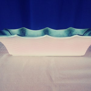 May include: A rectangular ceramic planter with a light pink interior and a wavy, light blue and green exterior.