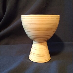 May include: A white ceramic vase with brown stripes. The vase has a wide, round top and a narrow, cylindrical base.