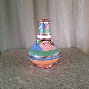 May include: A small, hand-painted ceramic vase with a bulbous body and a narrow neck. The vase is decorated with a colorful geometric pattern in shades of blue, green, pink, and brown.
