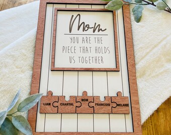 Puede incluir: Señal de madera con el texto "Mamá Eres La Pieza Que Nos Une" y un diseño de rompecabezas con los nombres Liam, Chantal, Mamá, Francois y Melanie.