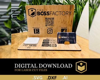 Op de afbeelding: Een houten toonbankdisplay met een bord waarop "The Boss Factory" staat en een logo van een berg met een opkomende zon. De stand heeft een witte vierkante kaartlezer, een visitekaartjeshouder en een bord met de tekst "Tap Here". De stand is versierd met logo's voor verschillende betaalmethoden, waaronder Visa, Mastercard en Apple Pay.