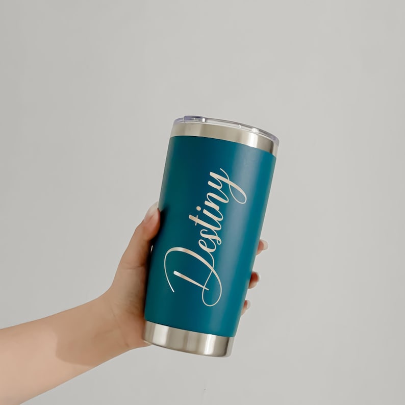 May include: Teal insulated tumbler with a silver rim and lid. The word "Destiny" is written in a cursive font on the side of the tumbler. The tumbler is cylindrical and appears to be made of stainless steel.