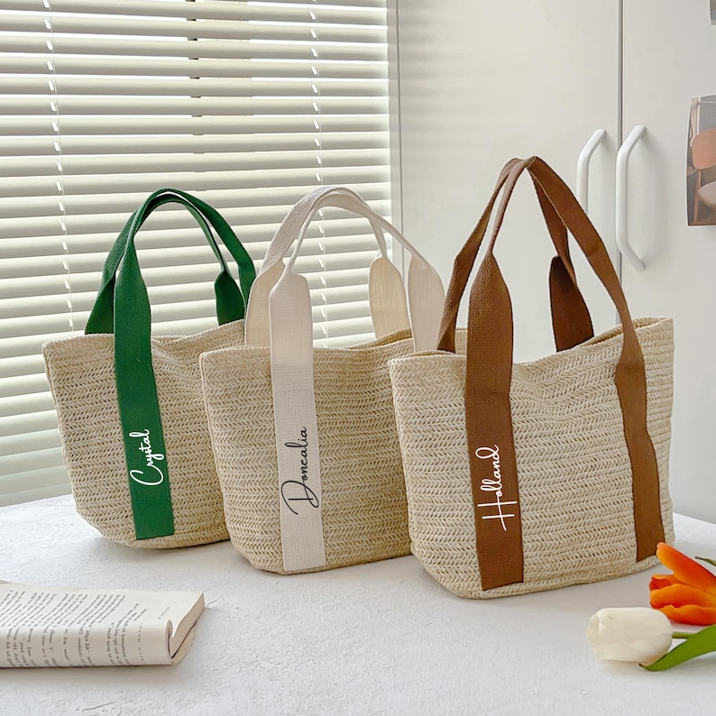 May include: Three woven straw tote bags with different colored handles and straps. The bags have the names "Crystal", "Doncalia", and "Holland" printed on the straps. The bags are beige with green, white, and brown straps.