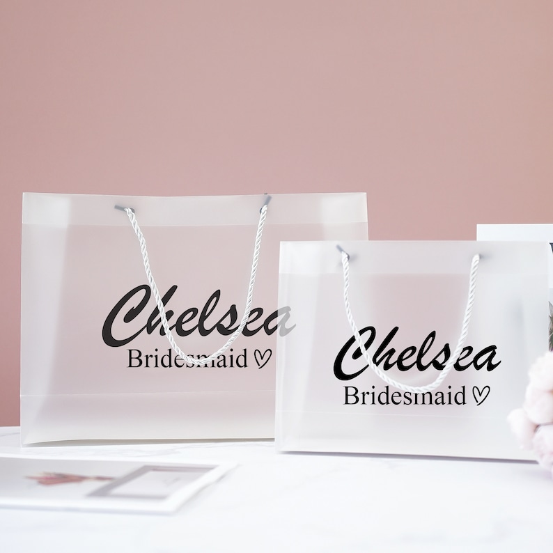 May include: Two clear plastic gift bags with white handles. The bags have the name "Chelsea" and the word "Bridesmaid" printed on them.