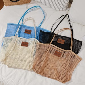 Puede incluir: Cuatro bolsas de malla en azul, crema, negro y marr&oacute;n, cada una con un parche rectangular de cuero. La bolsa azul tiene un asa azul, la bolsa crema tiene un asa crema, la bolsa negra tiene un asa negra y la bolsa marr&oacute;n tiene un asa marr&oacute;n. Las bolsas est&aacute;n sobre una superficie blanca.