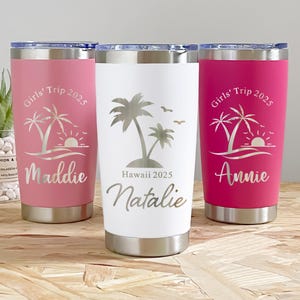 Peut inclure: Trois gobelets de voyage en acier inoxydable roses et blancs, chacun avec un couvercle et une base argentés. Les gobelets sont personnalisés avec des noms et un motif tropical avec des palmiers, un coucher de soleil et le texte "Girls' Trip 2025."