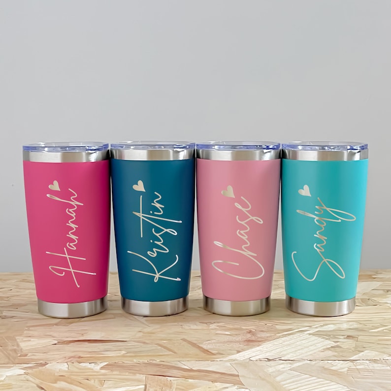 May include: Four stainless steel tumblers in pink, teal, and blue, each with a name in a cursive font. The names are Hannah, Kristin, Chase, and Sandy. Each tumbler has a silver lid and base, with a small heart graphic.