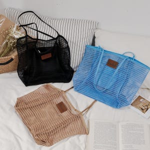 Puede incluir: Tres bolsas de malla en negro, azul y beige, cada una con una etiqueta de polipiel marr&oacute;n que dice "Rachel". Las bolsas tienen asas largas y est&aacute;n dise&ntilde;adas para transportar objetos. Las bolsas est&aacute;n sobre una superficie blanca.
