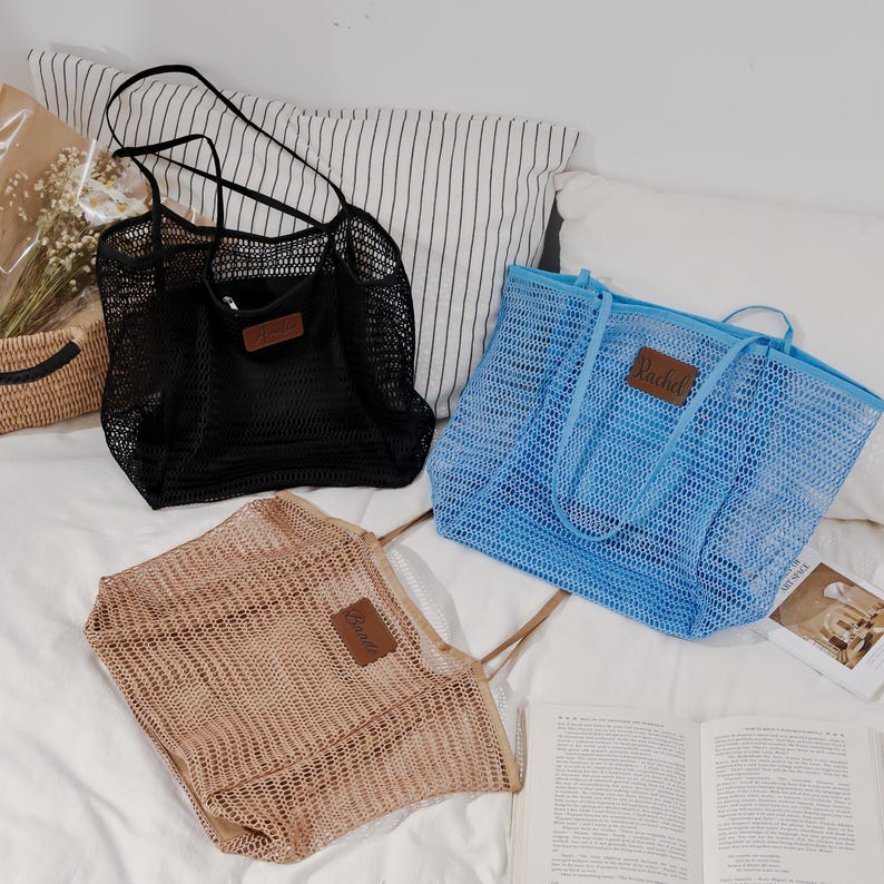 Puede incluir: Tres bolsas de malla en negro, azul y beige, cada una con una etiqueta de polipiel marr&oacute;n que dice "Rachel". Las bolsas tienen asas largas y est&aacute;n dise&ntilde;adas para transportar objetos. Las bolsas est&aacute;n sobre una superficie blanca.
