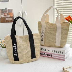 May include: Two woven straw tote bags. One has black handles and the name "Amanda" in white script. The other has cream-colored handles and the name "Natalia" in white script. Both bags are rectangular with a woven design.