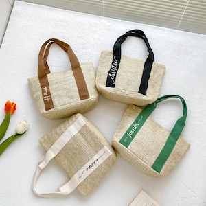 May include: Four woven straw tote bags with different colored handles and personalized text. The handles are brown, black, white, and green. The text on the bags reads "Holland", "christie", "hanna", and "jennifer".