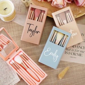 Könnte beinhalten: Drei personalisierte Make-up-Pinselsets mit einem Spiegel. Die Sets sind in Rosa, Blau und Beige mit den Namen Taylor, Emily und Jan darauf.