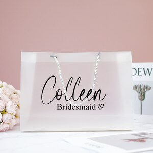 May include: A clear plastic gift bag with white rope handles. The bag has the text "Colleen Bridesmaid" printed on it.