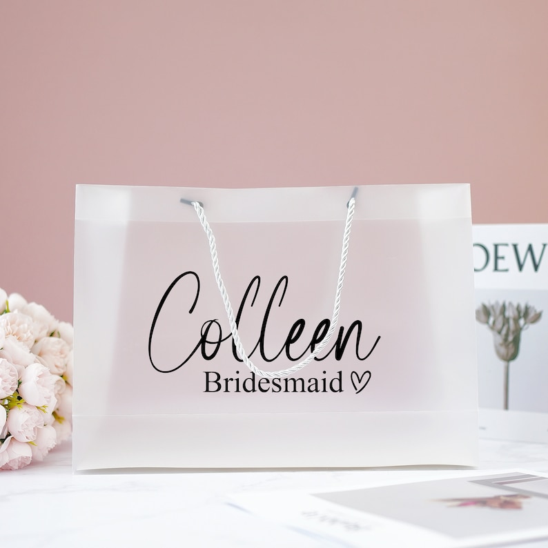 May include: A clear plastic gift bag with white rope handles. The bag has the text "Colleen Bridesmaid" printed on it.
