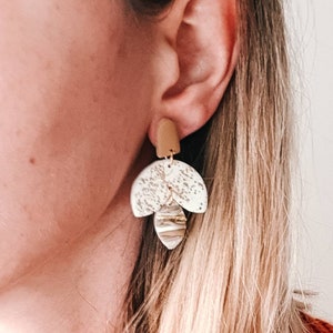 Op de afbeelding: Een paar oorhangers met een geometrisch ontwerp in wit en goud. De oorhangers zijn gemaakt van klei en hebben een textuur.