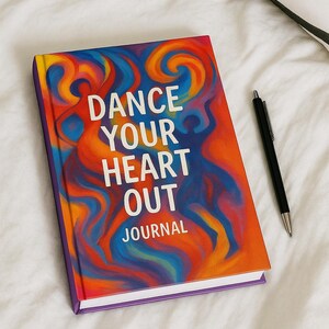 May include: A journal with a colorful abstract design on the cover, featuring the words "DANCE YOUR HEART OUT JOURNAL" in white. A black pen rests beside the journal on a white surface. The cover has a vibrant mix of orange, blue, and yellow.