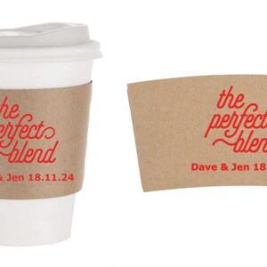 Pu&ograve; includere: Una tazza da caff&egrave; di carta bianca con coperchio e una fascetta di carta marrone. La fascetta e la tazza presentano la scritta "the perfect blend" in rosso, insieme ai nomi "Dave & Jen" e la data 18.11.24.