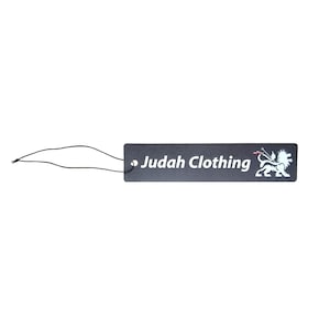 Könnte beinhalten: Ein rechteckiges schwarzes Kleidungsetikett mit dem Text "Judah Clothing" in Weiß. Ein weißes Löwenemblem befindet sich auf der rechten Seite des Etiketts. Ein schwarzer Faden ist am Etikett befestigt.