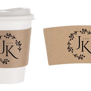 Pu&ograve; includere: Una tazza da caff&egrave; di carta bianca con coperchio e una manica di carta marrone. La manica e una manica aggiuntiva mostrano un design a ghirlanda floreale nera con le lettere "JK" e la parola "AND".