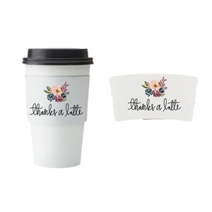 Pu&ograve; includere: Una tazza da caff&egrave; da viaggio bianca con coperchio nero e un motivo floreale sulla manica. La manica presenta la scritta "thanks a latte" in corsivo. Viene mostrata anche una manica separata con lo stesso design.