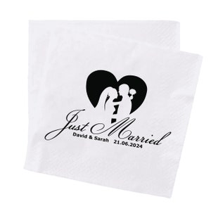 May include: White paper napkin with a black heart-shaped design featuring a couple's silhouette. The words "Just Married" are written in elegant script, along with the names "David & Sarah" and the date "21.06.2024".