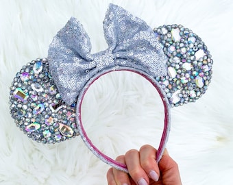 Op de afbeelding: Zilveren Minnie Mouse oren met pailletten, een grote zilveren strik en iriserende strass steentjes.