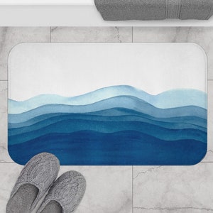 May include: A blue and white watercolor bath mat with a design of abstract waves. The mat is on a light gray tiled floor.