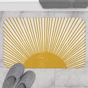 May include: A yellow and white bath mat with a sunburst design. The sunburst is a half circle with yellow rays radiating out from the center.