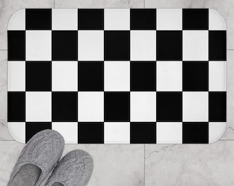 May include: Black and white checkered bath mat with a geometric pattern. The mat is made of a soft, absorbent material and is perfect for adding a touch of style to any bathroom.