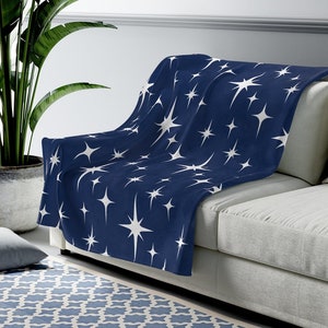 May include: A navy blue throw blanket with a white star pattern. The blanket is draped over a light gray couch.