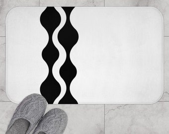 May include: White bath mat with a black wavy design on the left side. The mat is on a tiled floor.