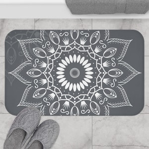 May include: A gray bath mat with a white mandala design. The mandala is intricate and detailed, with a central flower-like pattern.