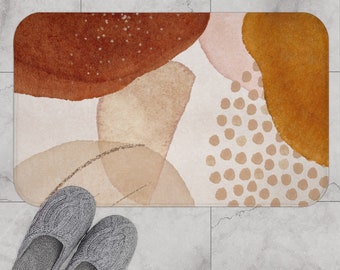 May include: Abstract bath mat with a white background and brown, orange, and pink watercolor shapes. The mat has a polka dot pattern in the center.