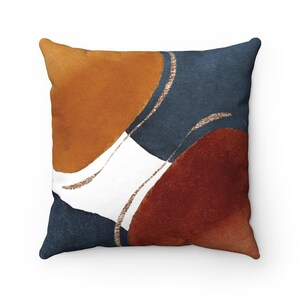 May include: A square cushion with an abstract design featuring overlapping circles in shades of burnt orange, rust, navy blue, and white with gold glitter accents.