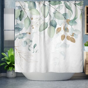 May include: White shower curtain with a watercolor design of green and gold eucalyptus leaves. The leaves are in various shades of green and blue, with gold glitter accents. The curtain is hanging in a bathroom.